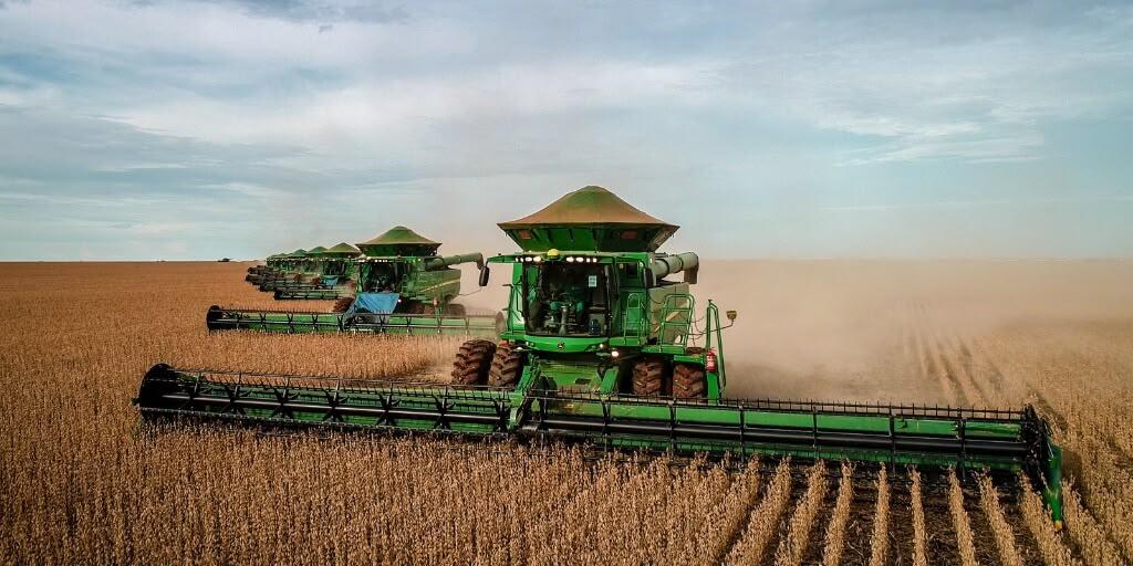 A fleet of combine harvesters working in formation across a soybean field.