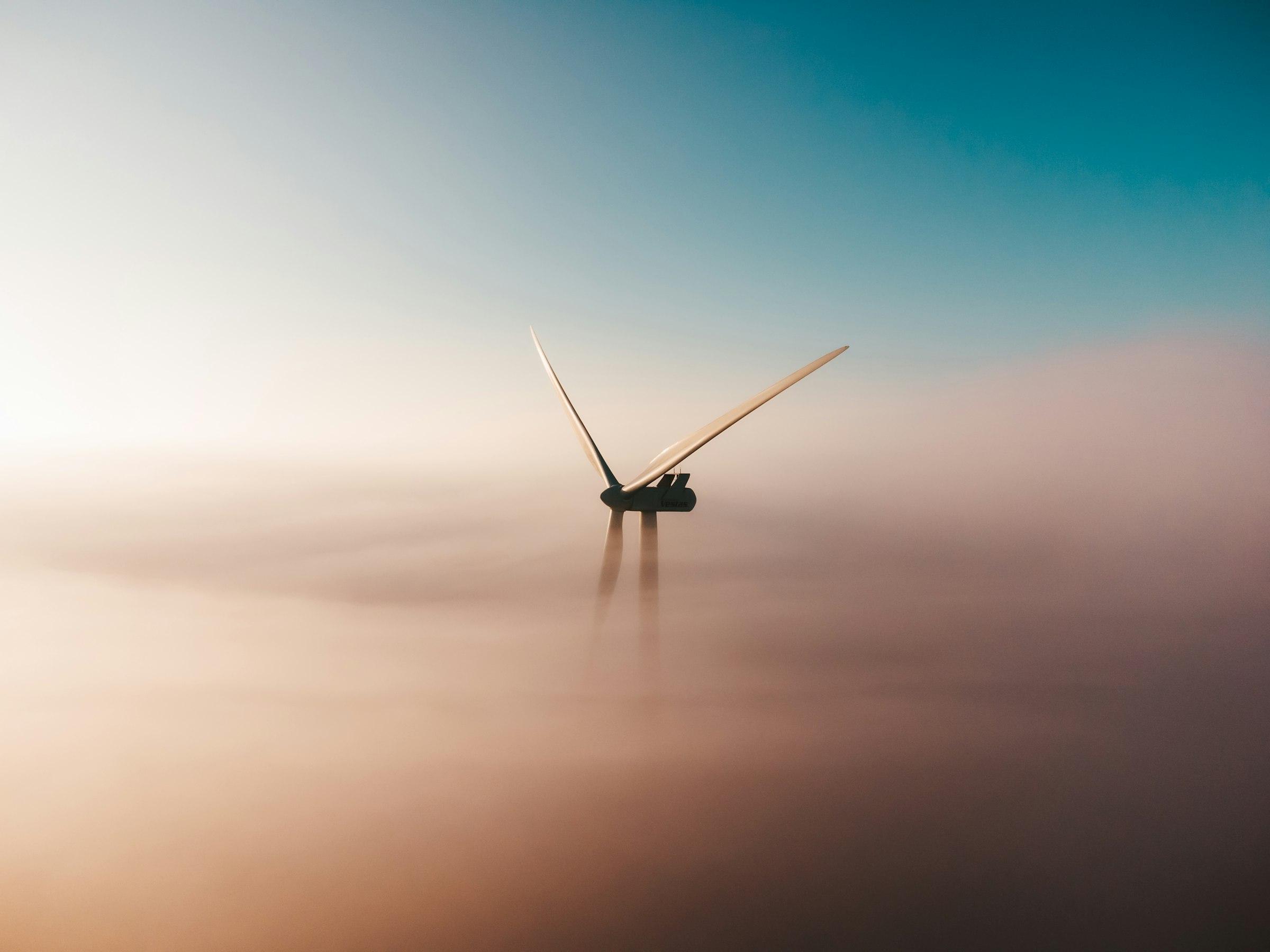 A wind turbine rising above morning fog.