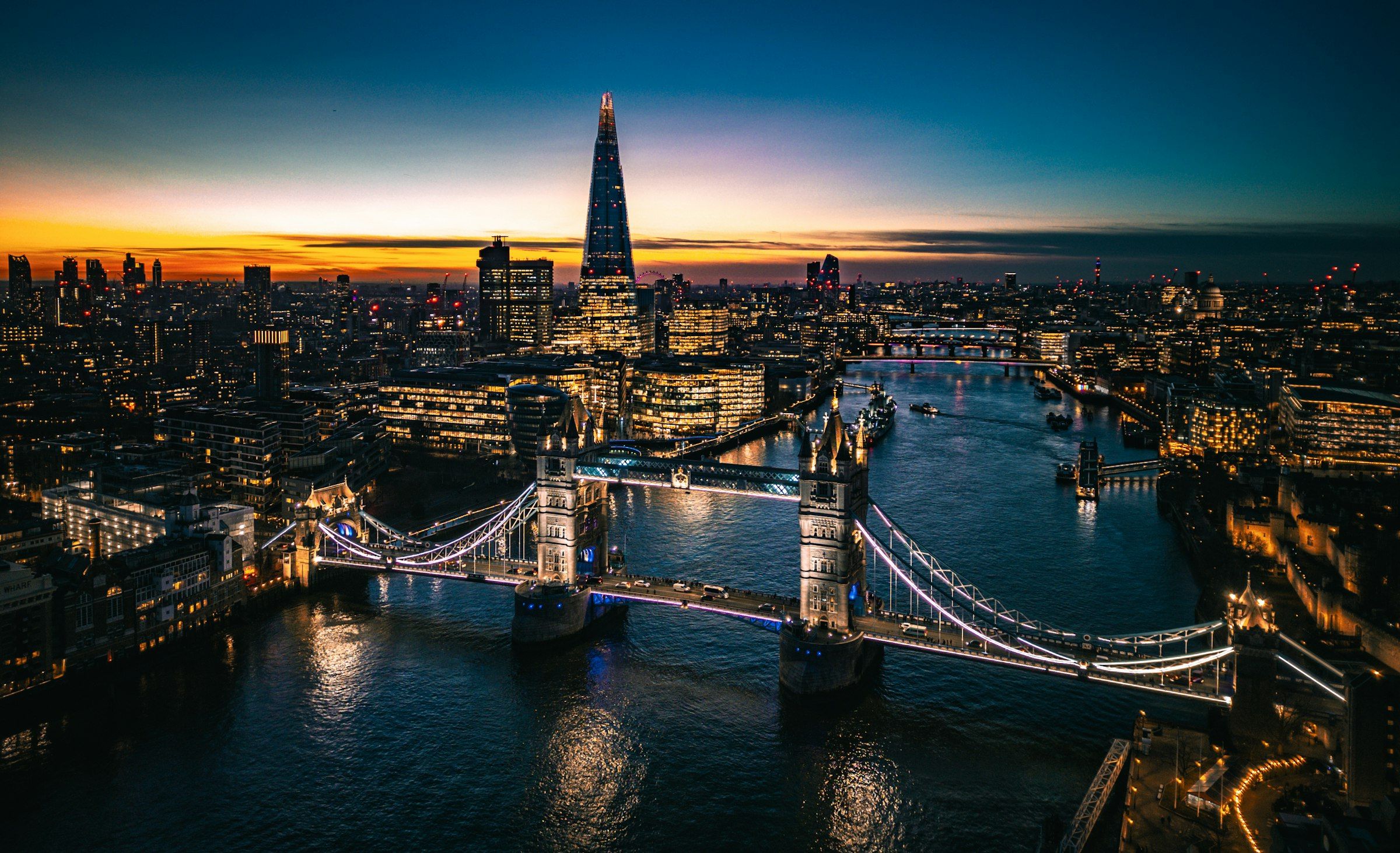 Aerial view of the River Thames and Tower Bridge at dusk, with the City of London beyond.